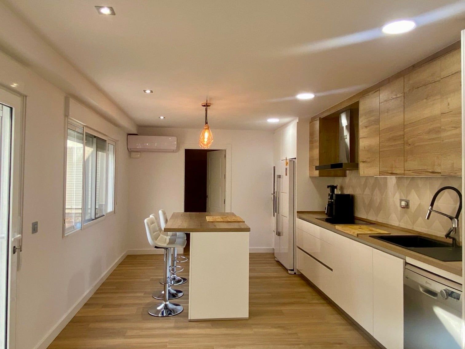Cocina lineal con isla, frentes de madera clara y muebles bajos blancos