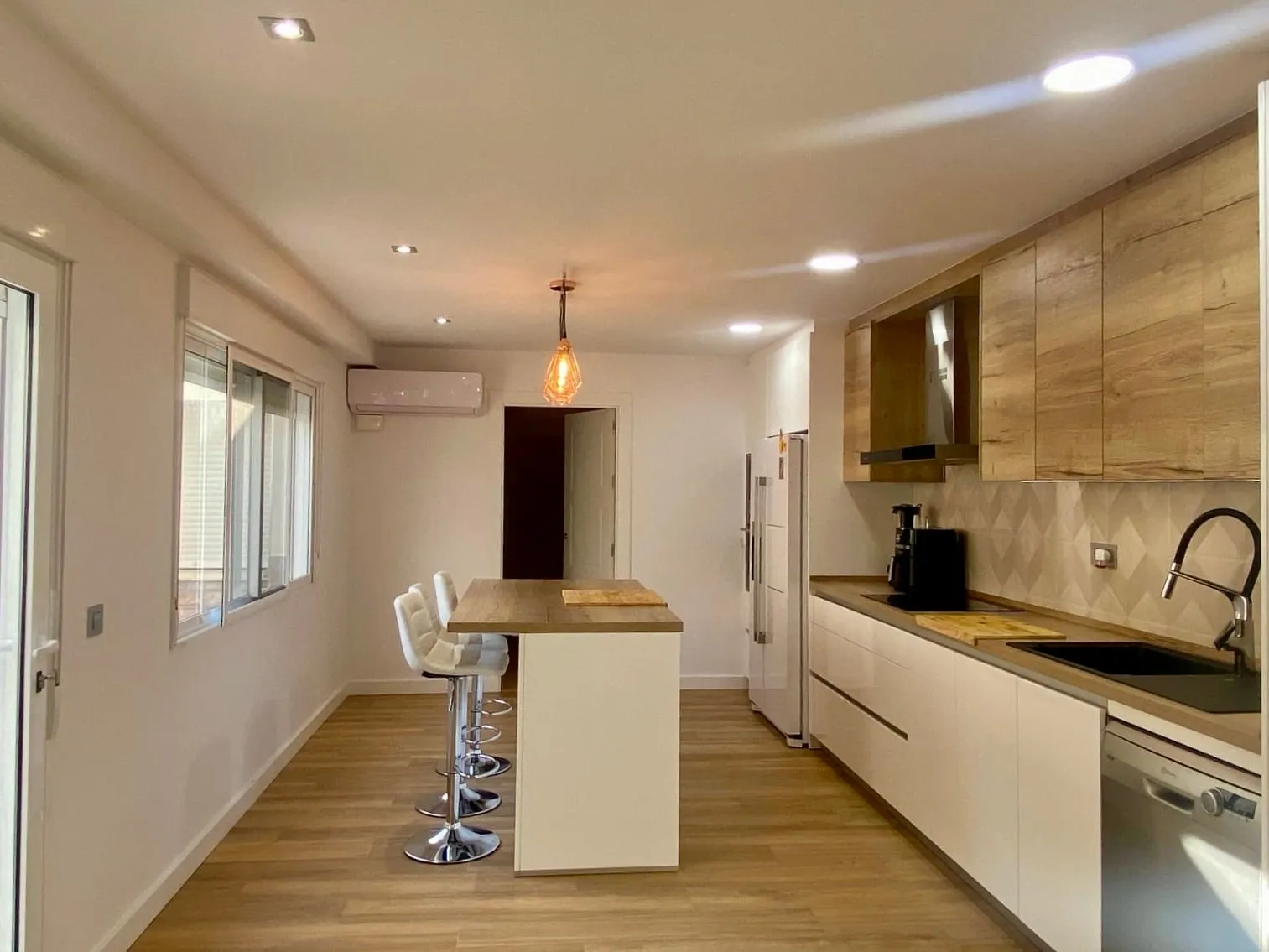 Cocina lineal con isla, frentes de madera clara y muebles bajos blancos