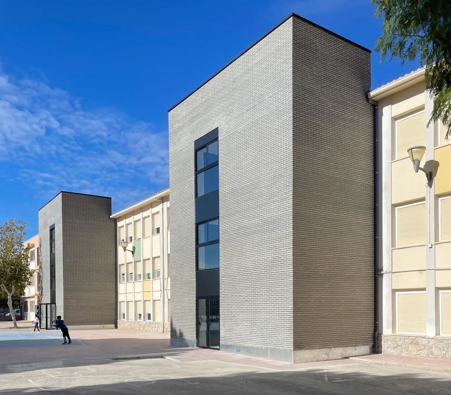 Volúmenes nuevos de ladrillo gris adosados al edificio existente del colegio