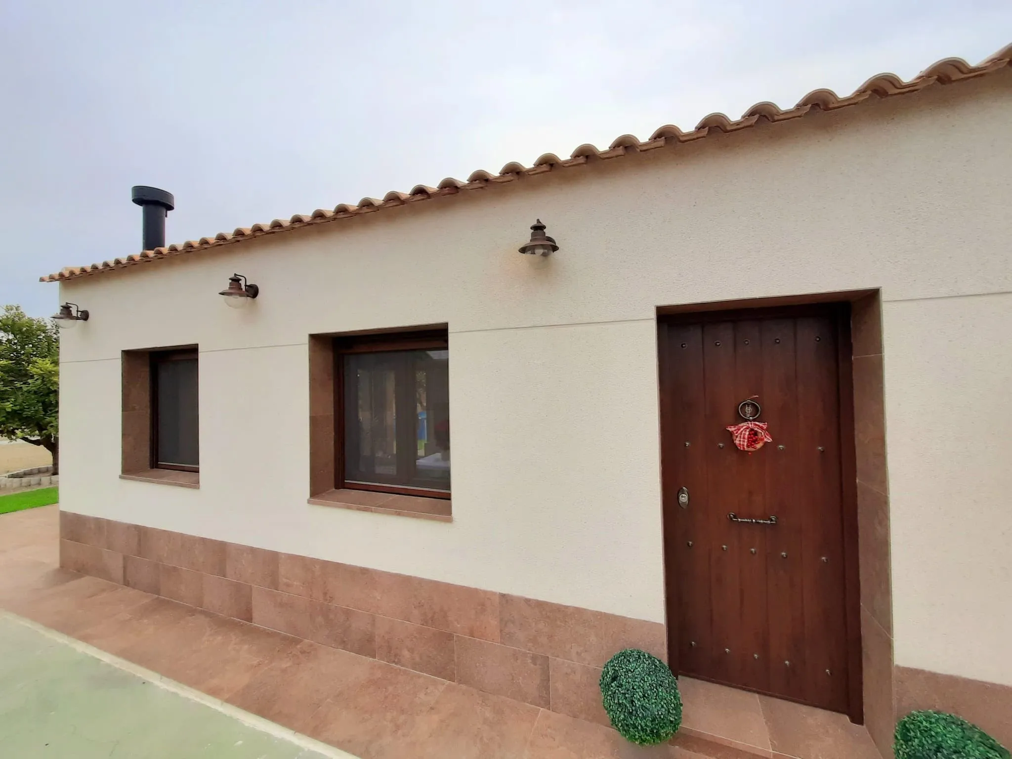 Fachada blanca con zócalo cerámico, puerta de madera y alero de teja