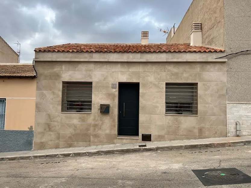 Vista frontal de la fachada con aplacado, rejas y cubierta de teja
