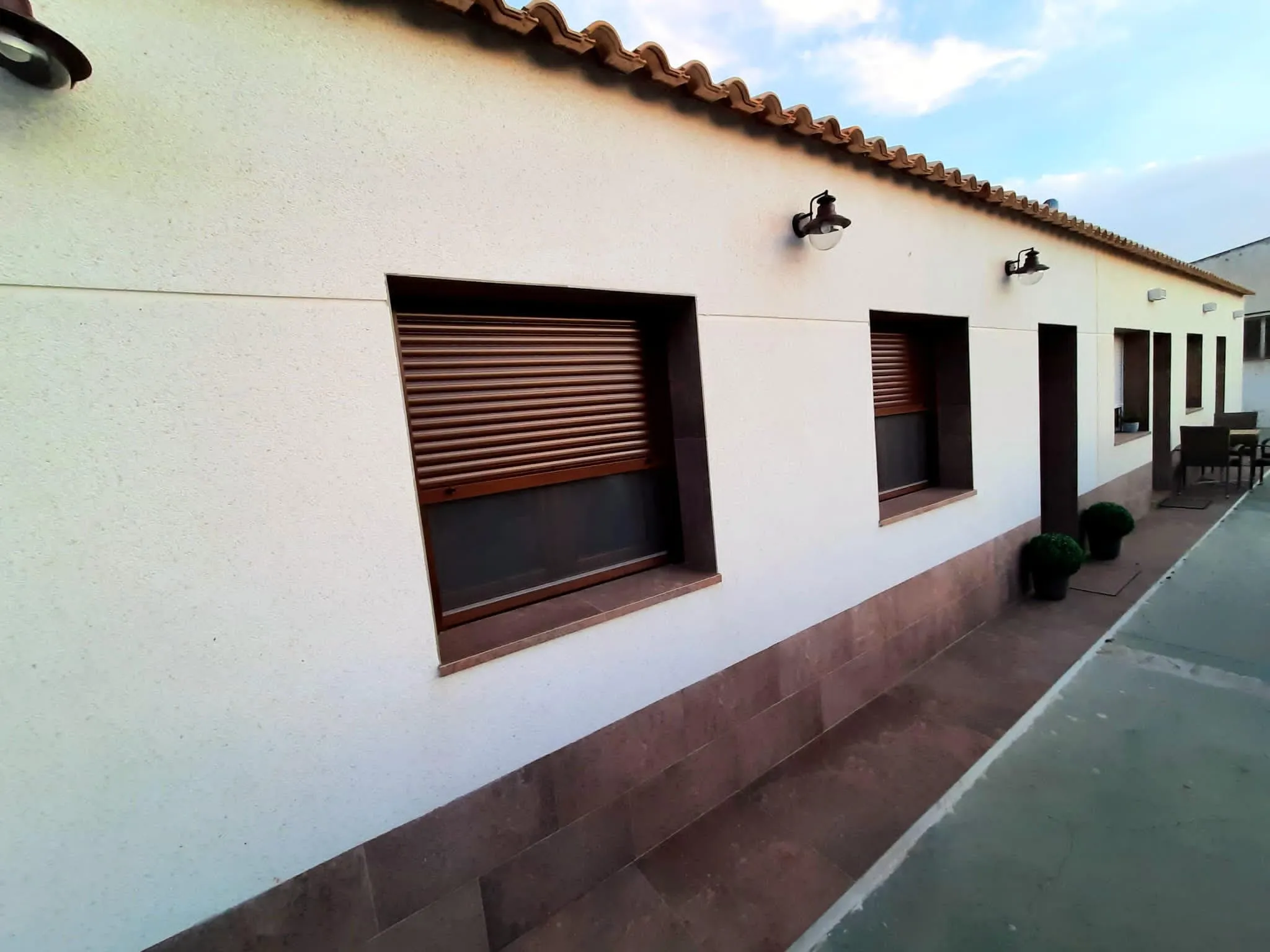 Fachada lateral con ventanas enmarcadas y zócalo cerámico junto al paso pavimentado